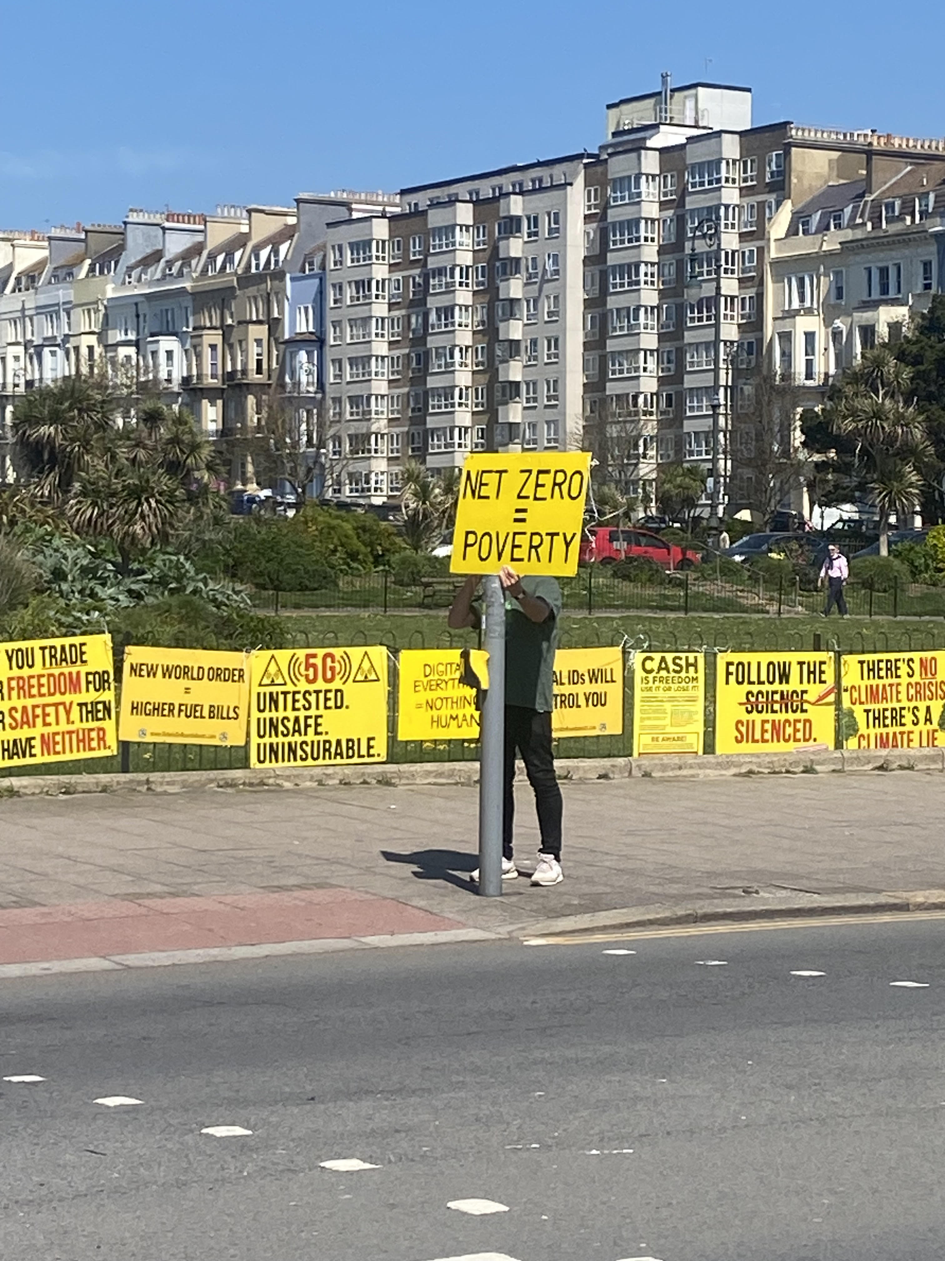 A mans face covered by a sign that reads 'net zero = fuel poverty"