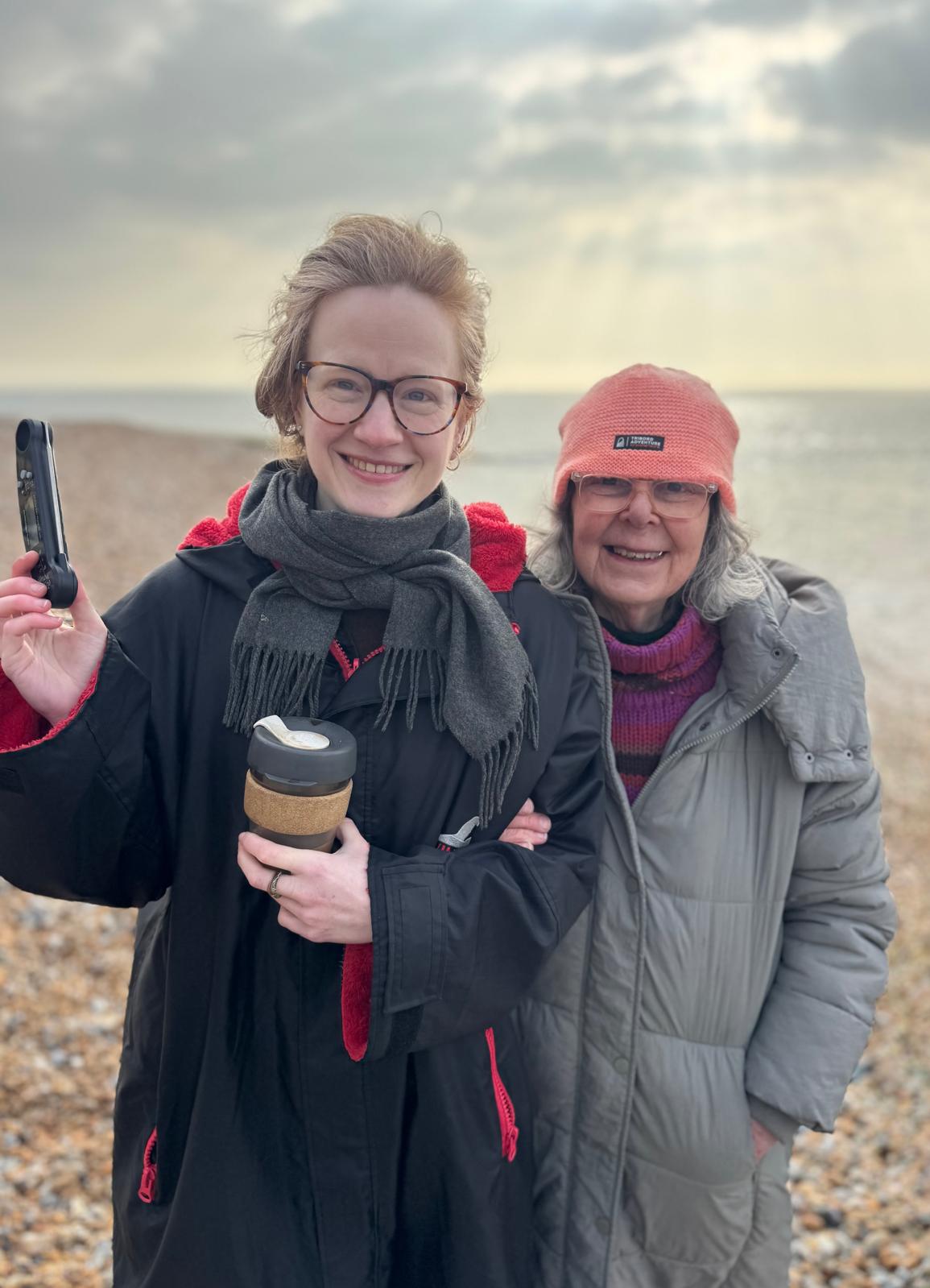 Two women stand in front of the sea one holding a thermometer
